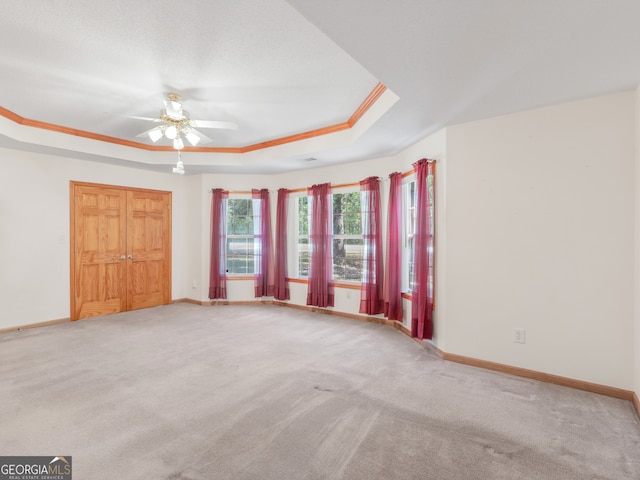 unfurnished bedroom with carpet flooring, ceiling fan, a raised ceiling, a closet, and ornamental molding