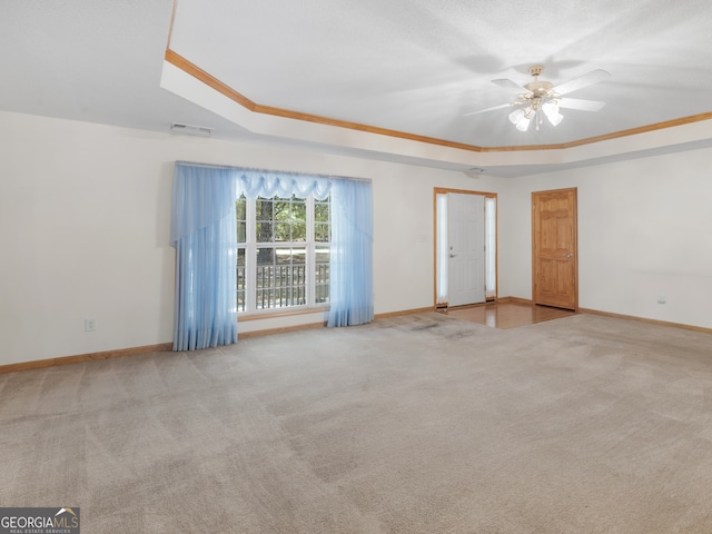 carpeted empty room with a tray ceiling, crown molding, and ceiling fan