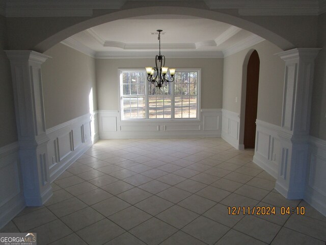 unfurnished dining area with arched walkways, light tile patterned floors, a raised ceiling, a decorative wall, and an inviting chandelier