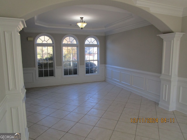 unfurnished room featuring light tile patterned floors, decorative columns, arched walkways, a tray ceiling, and crown molding