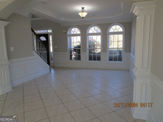 tiled spare room featuring a raised ceiling, decorative columns, crown molding, and an inviting chandelier