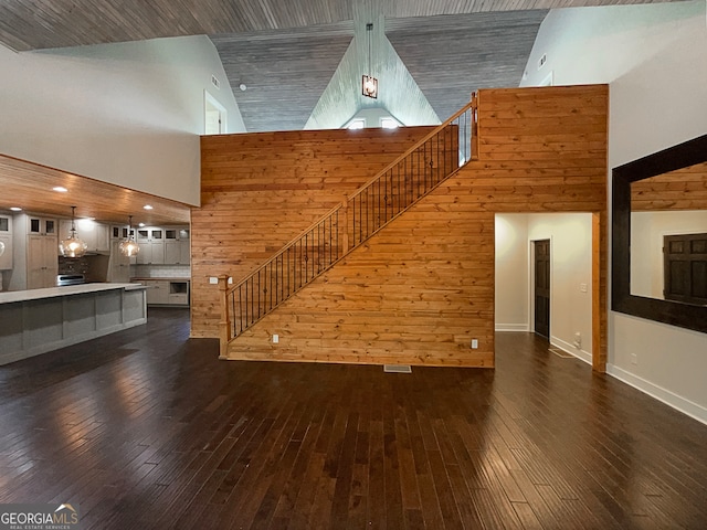 unfurnished living room featuring high vaulted ceiling, wood walls, and dark hardwood / wood-style floors