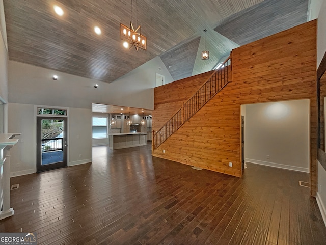 unfurnished living room featuring high vaulted ceiling, wood walls, a notable chandelier, and dark hardwood / wood-style flooring