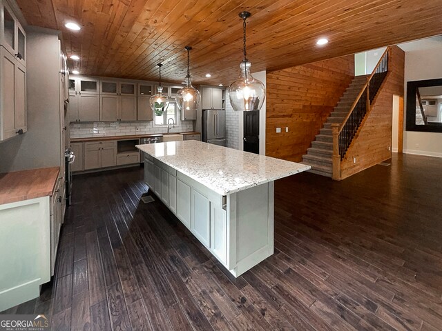 kitchen featuring stainless steel refrigerator, wood walls, dark hardwood / wood-style flooring, pendant lighting, and a spacious island