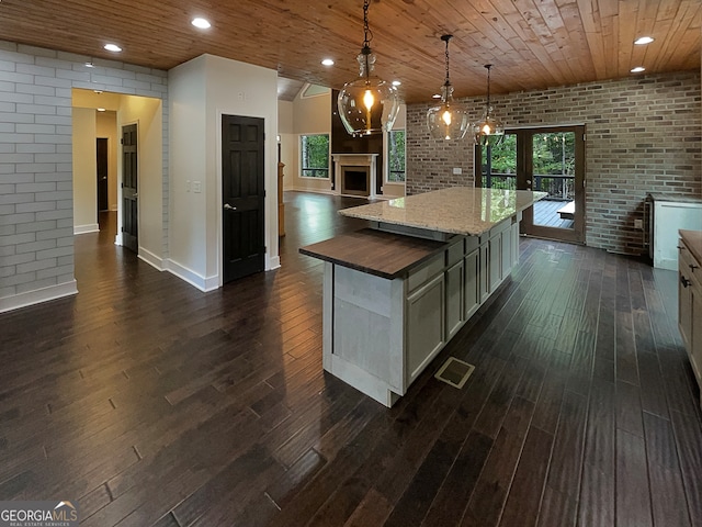 kitchen with a kitchen island, brick wall, decorative light fixtures, plenty of natural light, and dark hardwood / wood-style floors