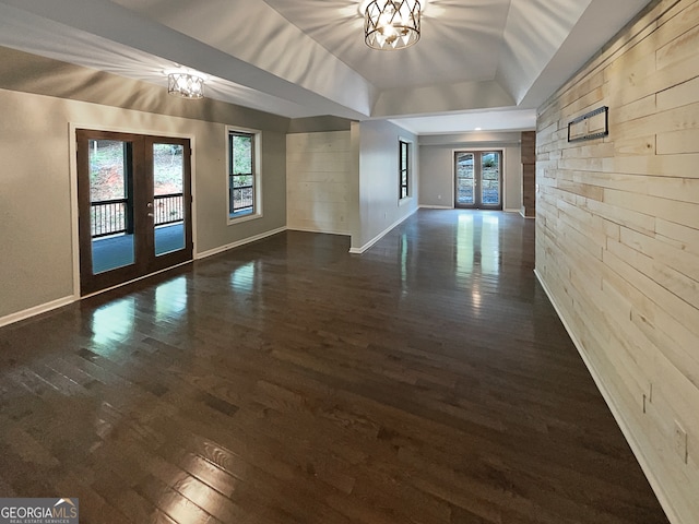 empty room featuring dark wood-type flooring, a notable chandelier, lofted ceiling, wooden walls, and french doors