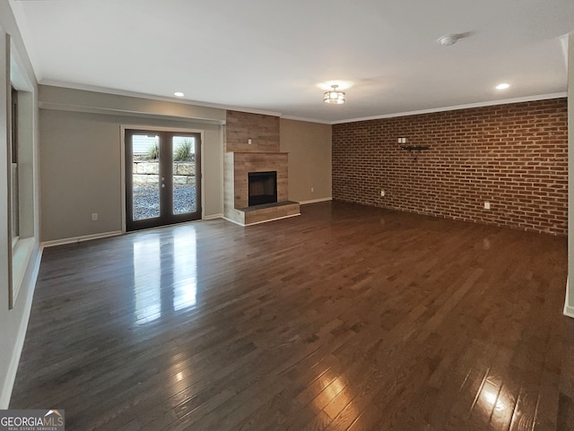 unfurnished living room featuring brick wall, french doors, dark hardwood / wood-style floors, a fireplace, and crown molding