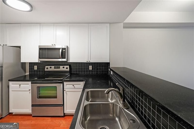 kitchen featuring appliances with stainless steel finishes, a sink, white cabinets, light wood-style flooring, and decorative backsplash
