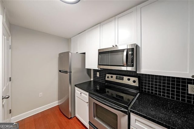 kitchen featuring stainless steel appliances, white cabinetry, dark countertops, light wood finished floors, and backsplash