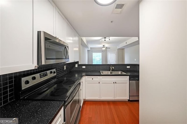 kitchen featuring stainless steel appliances, a sink, ceiling fan, light wood-style floors, and dark countertops