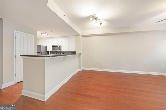 kitchen featuring appliances with stainless steel finishes, white cabinets, a peninsula, wood finished floors, and baseboards