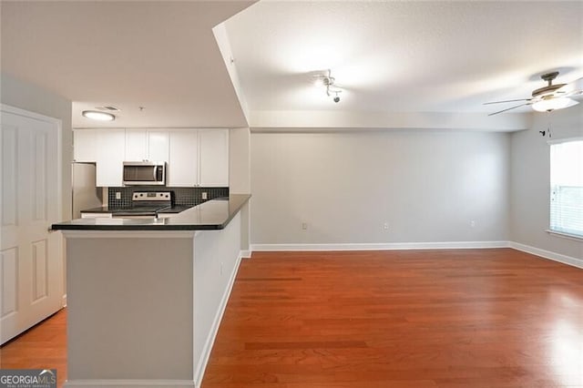 kitchen with stainless steel appliances, white cabinets, dark countertops, a peninsula, and a ceiling fan