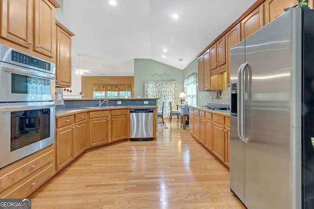 kitchen with stainless steel appliances, a peninsula, a sink, vaulted ceiling, and light wood-type flooring