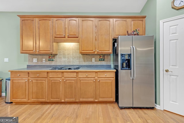 kitchen featuring brown cabinets, decorative backsplash, black gas stovetop, light wood-type flooring, and stainless steel fridge