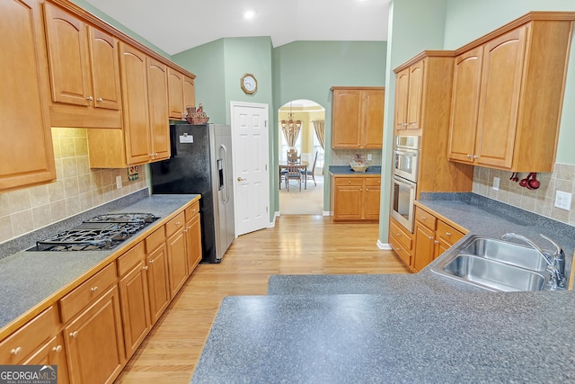 kitchen with arched walkways, lofted ceiling, light wood-style flooring, a sink, and appliances with stainless steel finishes