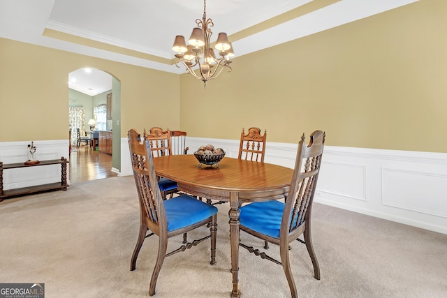 dining room featuring arched walkways, a raised ceiling, light carpet, wainscoting, and a chandelier