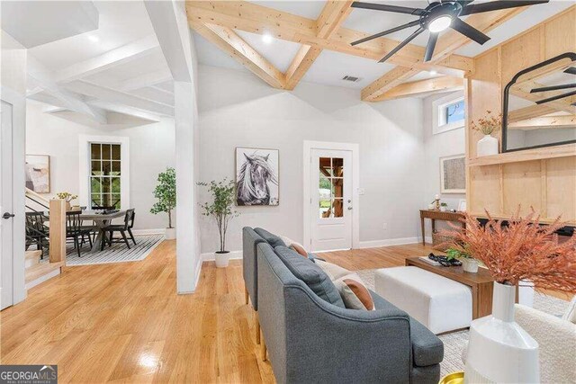 living room featuring light wood-type flooring, beamed ceiling, coffered ceiling, a high ceiling, and ceiling fan