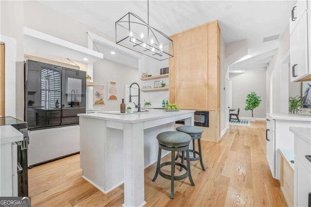 kitchen featuring white cabinetry, an island with sink, a breakfast bar area, light hardwood / wood-style flooring, and decorative light fixtures