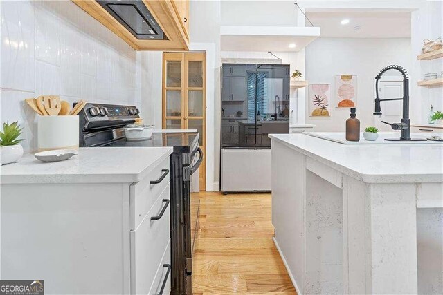 kitchen with black electric range, light hardwood / wood-style flooring, and white cabinets