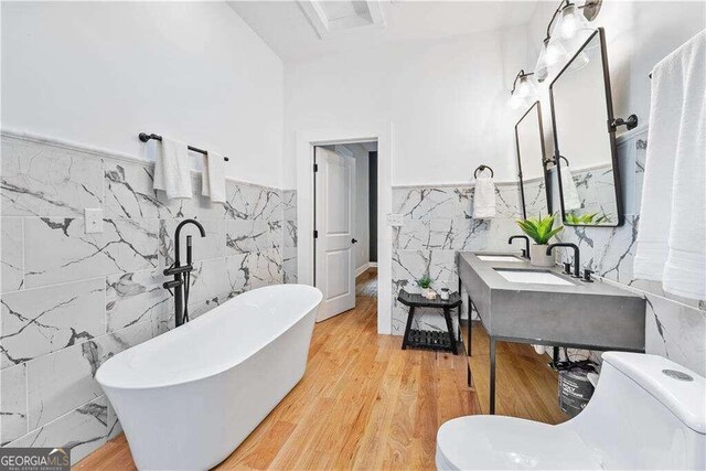 bathroom featuring wood-type flooring, tile walls, toilet, and a washtub