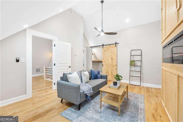 living room with light hardwood / wood-style flooring, ceiling fan, high vaulted ceiling, and a barn door