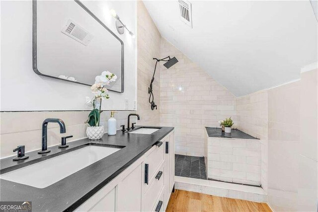 bathroom with tile walls, vaulted ceiling, tiled shower, vanity, and wood-type flooring