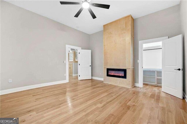 unfurnished living room featuring ceiling fan, light hardwood / wood-style floors, high vaulted ceiling, and a large fireplace