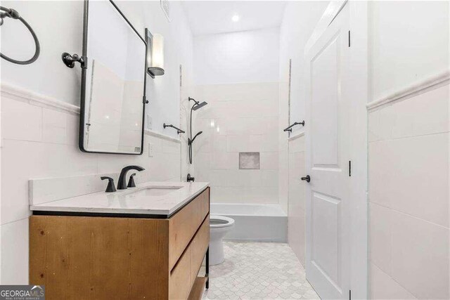 full bathroom featuring tiled shower / bath, vanity, tile walls, and toilet