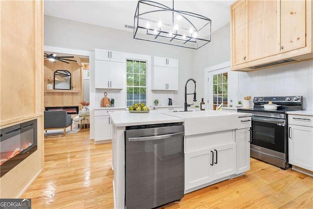 kitchen with pendant lighting, a kitchen island with sink, white cabinets, light hardwood / wood-style flooring, and stainless steel appliances