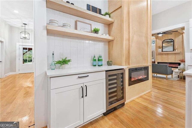 bar with light wood-type flooring, hanging light fixtures, white cabinetry, and beverage cooler