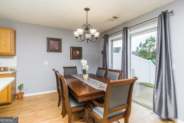 dining area with an inviting chandelier, light wood-type flooring, and a textured ceiling