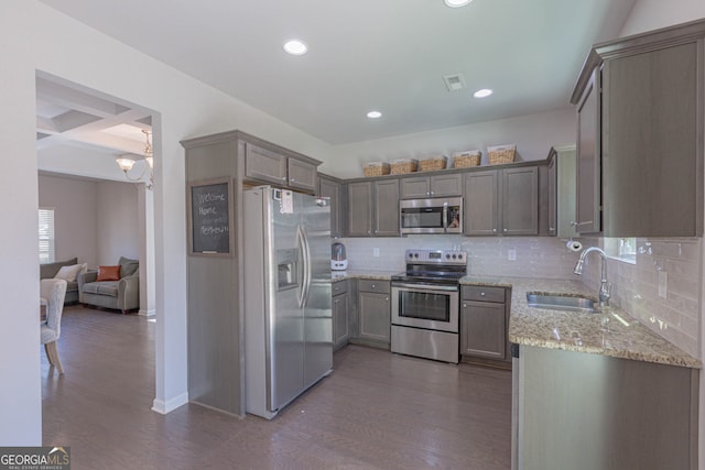 kitchen featuring sink, stainless steel appliances, dark hardwood / wood-style floors, light stone countertops, and decorative backsplash