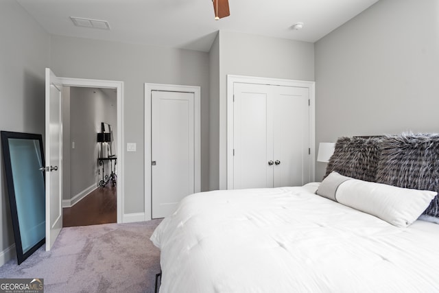 carpeted bedroom with ceiling fan and two closets