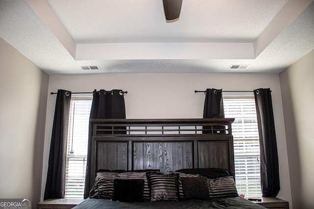 bedroom with ceiling fan, a tray ceiling, and multiple windows