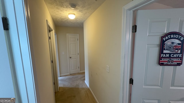 hallway with a textured ceiling and light colored carpet