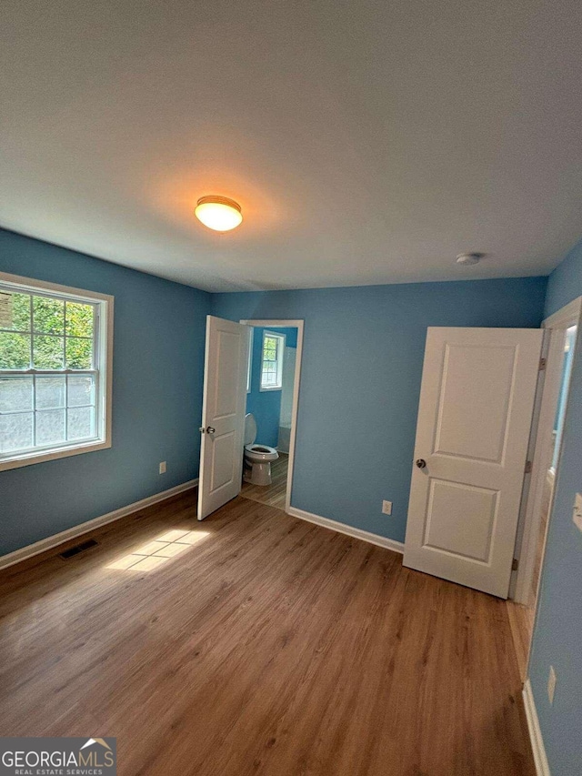 unfurnished bedroom with multiple windows, connected bathroom, and light hardwood / wood-style floors