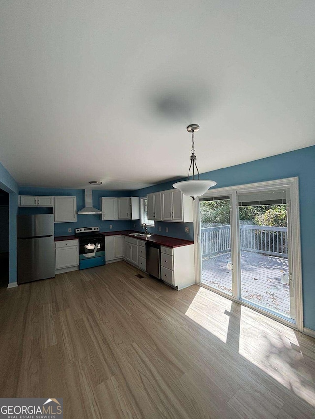 kitchen featuring pendant lighting, sink, wall chimney exhaust hood, appliances with stainless steel finishes, and light hardwood / wood-style floors