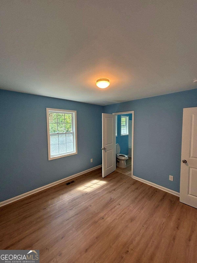 unfurnished bedroom with light hardwood / wood-style flooring and connected bathroom