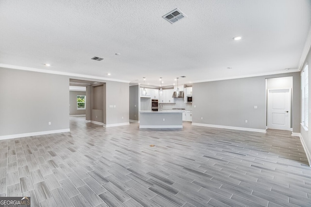 unfurnished living room with a textured ceiling, ornamental molding, and light hardwood / wood-style floors