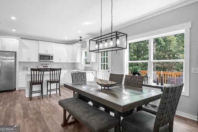 dining room with wood-type flooring, ornamental molding, sink, and a notable chandelier