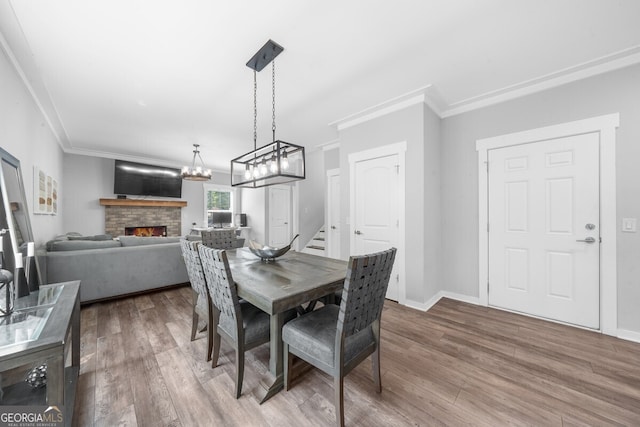 dining space featuring wood-type flooring, a stone fireplace, and crown molding