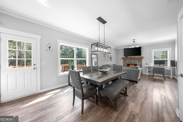 dining room featuring wood-type flooring, a stone fireplace, and ornamental molding