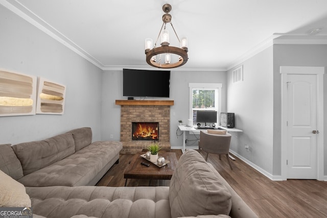 living room with crown molding, hardwood / wood-style floors, a brick fireplace, and a notable chandelier