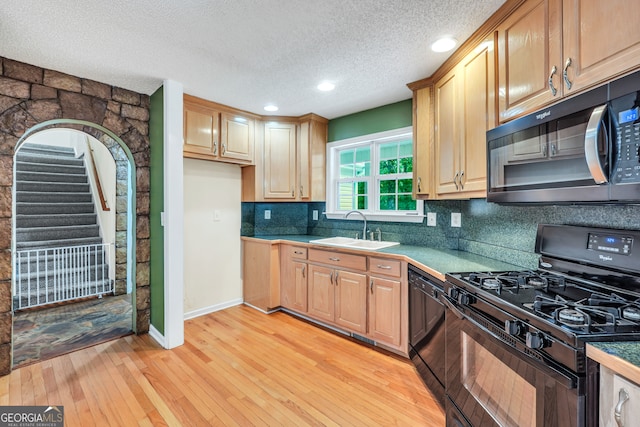 kitchen featuring a textured ceiling, sink, light hardwood / wood-style flooring, decorative backsplash, and black appliances