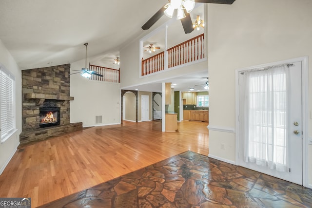 unfurnished living room featuring a stone fireplace, hardwood / wood-style flooring, sink, and high vaulted ceiling