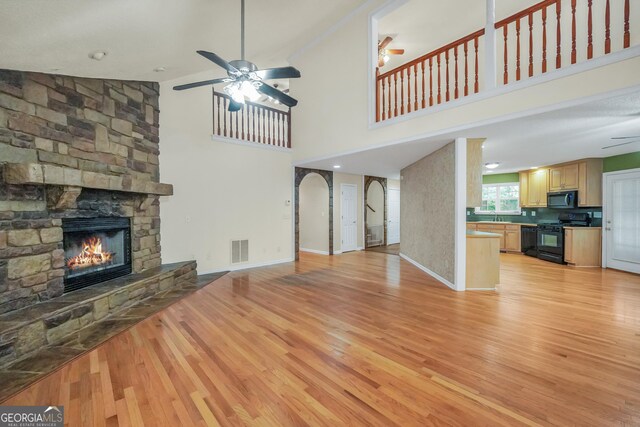 unfurnished living room with ceiling fan, a stone fireplace, hardwood / wood-style floors, and high vaulted ceiling