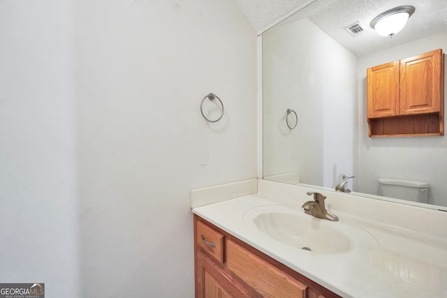 bathroom featuring a textured ceiling, vanity, and toilet