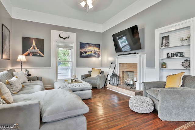 living room with built in shelves, ceiling fan, dark hardwood / wood-style floors, a fireplace, and crown molding