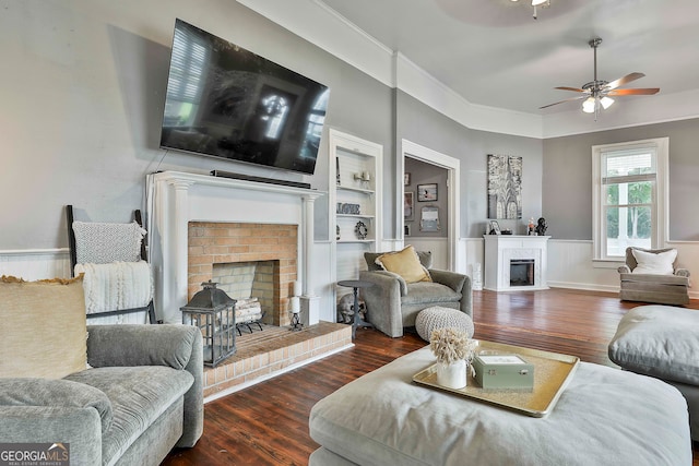 living room with built in shelves, ceiling fan, a fireplace, crown molding, and dark hardwood / wood-style flooring