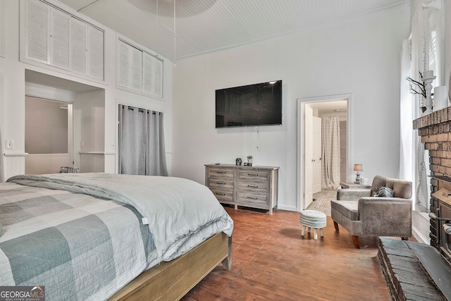 bedroom featuring a towering ceiling, a fireplace, and dark hardwood / wood-style flooring